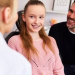 girl with braces discussing tooth alignment with her dentist and father.