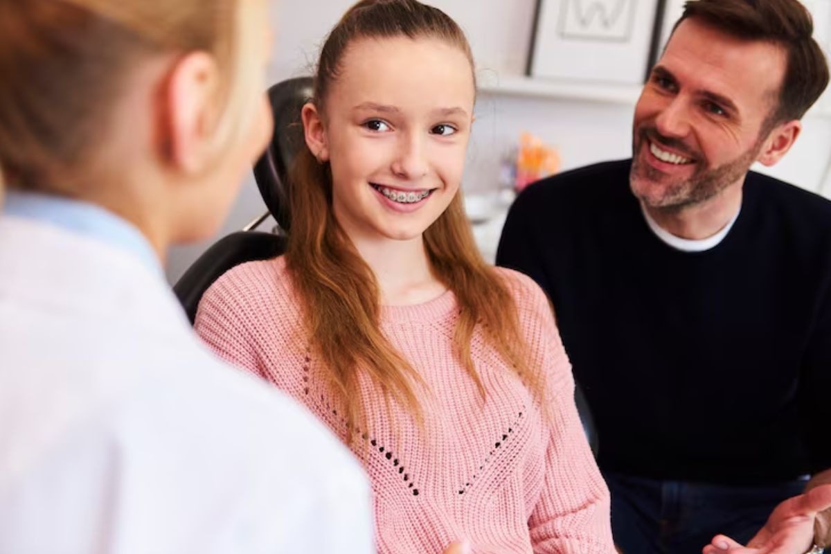 girl with braces discussing tooth alignment with her dentist and father.